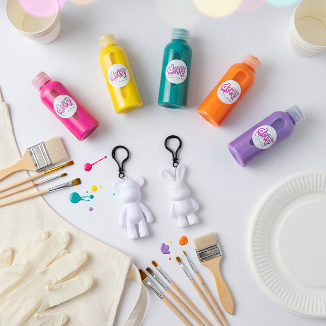 DubaiDripArt™ accessories flat-lay: paper cups, glitter vials, paper plates, brushes, keychains, mixing sticks, apron, and gloves
